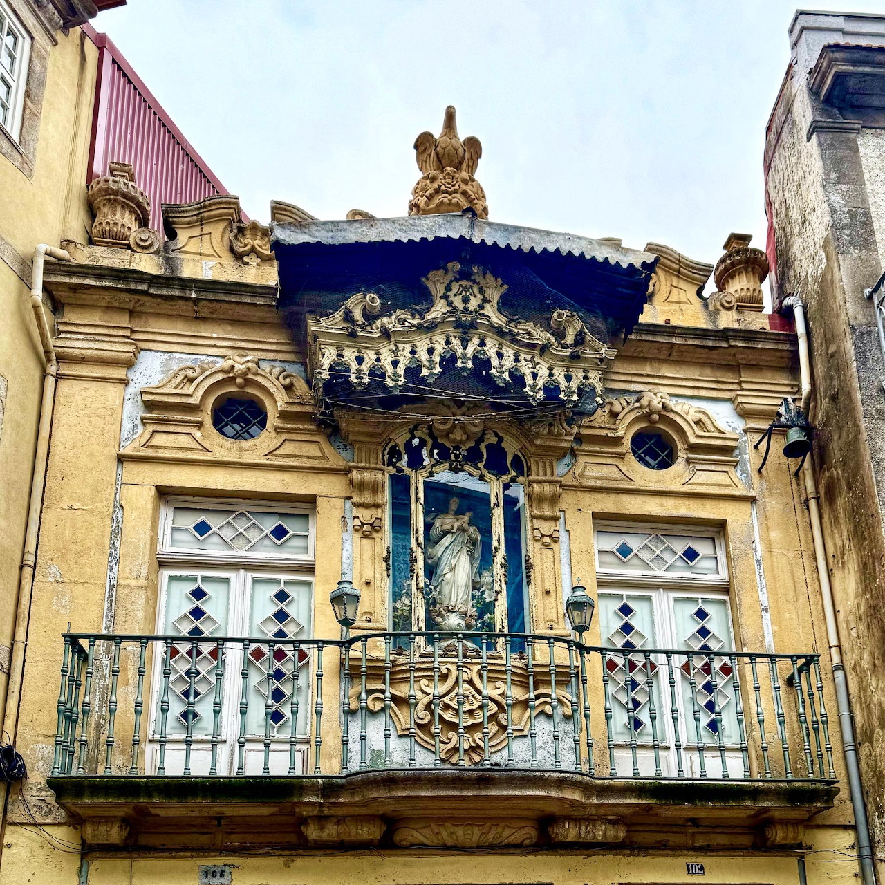 Yellow building facade with ornate balcony, blue awning, and iron railings in Porto