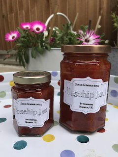 Two jars of rose hip jam with white labels on polka dot surface, purple flowers behind