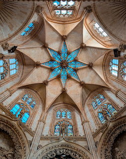 Looking up at Gothic cathedral ceiling with blue stained glass windows and star-shaped chandelier