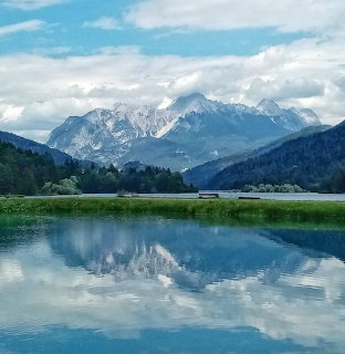 Snow-capped mountain range reflected in calm alpine lake with forest