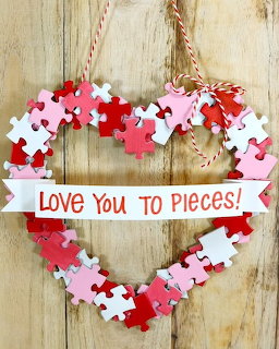 Heart wreath crafted from red, pink and white puzzle pieces with 'Love You to Pieces' banner on wooden backdrop