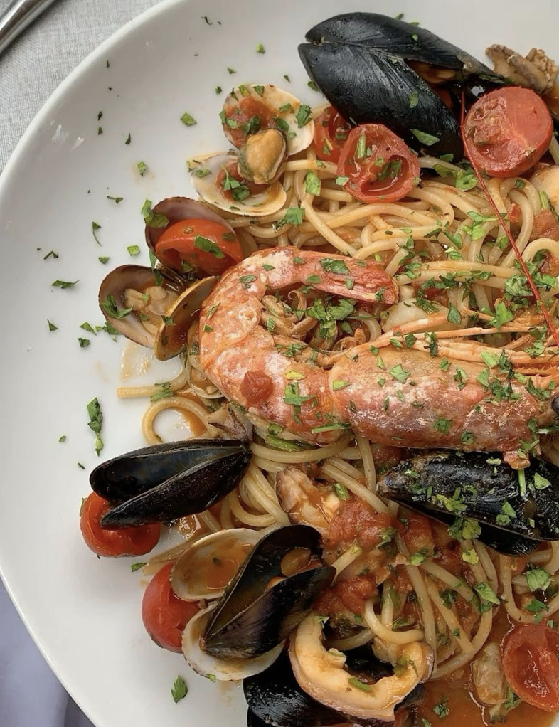 White bowl of seafood spaghetti with mussels, shrimp, clams, and tomatoes garnished with parsley