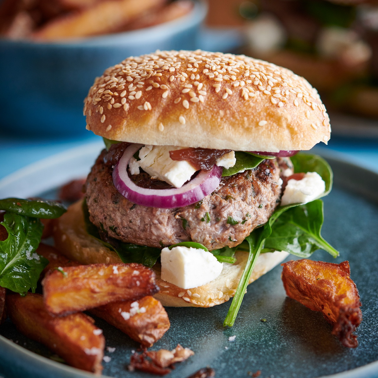 Gourmet burger with sesame bun and roasted potato wedges on a blue plate