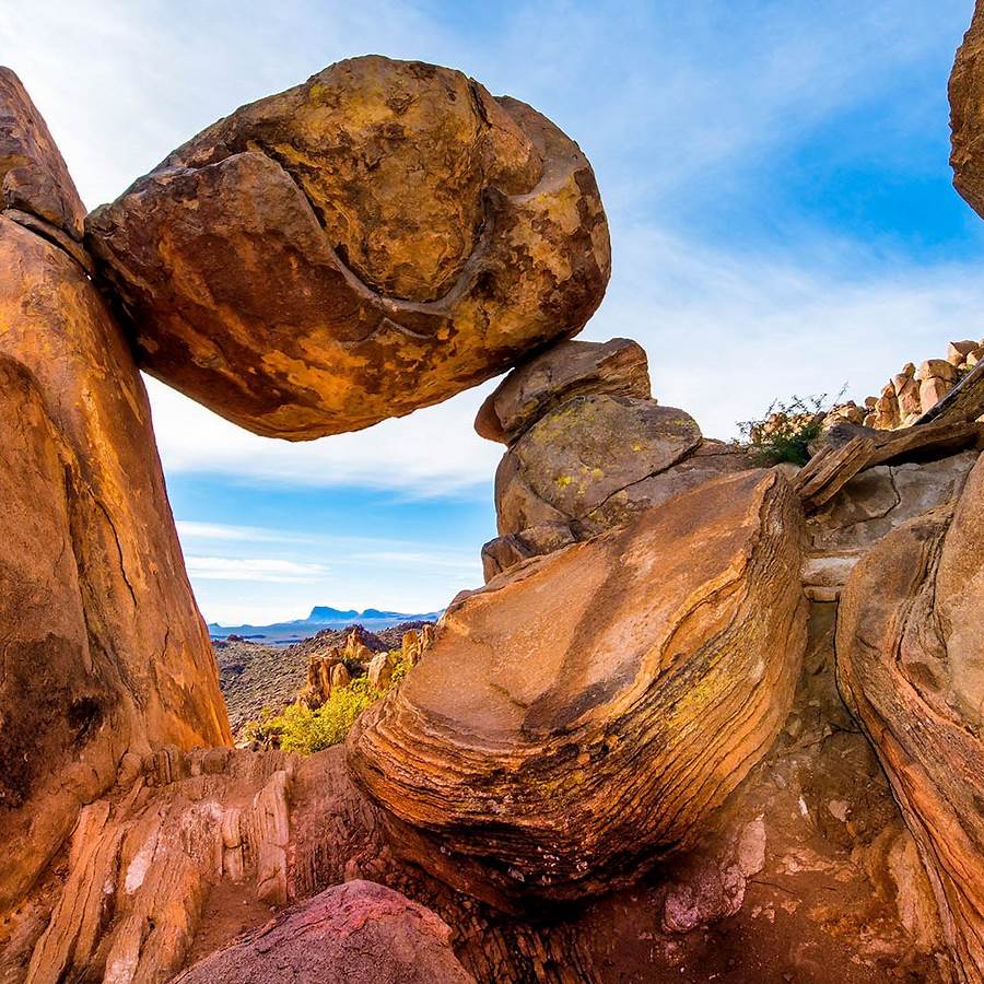 Boulder balanced on weathered rock formation in Texas desert with blue sky and mountains
