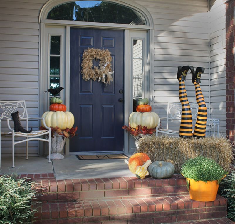 Halloween front porch with pumpkins, hay bales, witch legs, and a blue door with a wreath