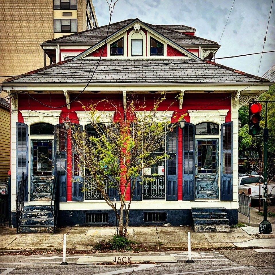 Victorian house with red trim, white siding, and young tree in front on city street