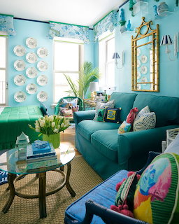 Bright blue living room with teal sofa, wall plates, colorful pillows, and round coffee table