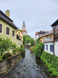 Canal running between colorful buildings in Český Krumlov with castle tower in background
