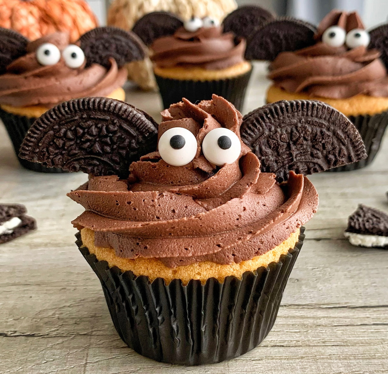 Chocolate cupcakes decorated as bats with frosting, candy eyes, and Oreo wings