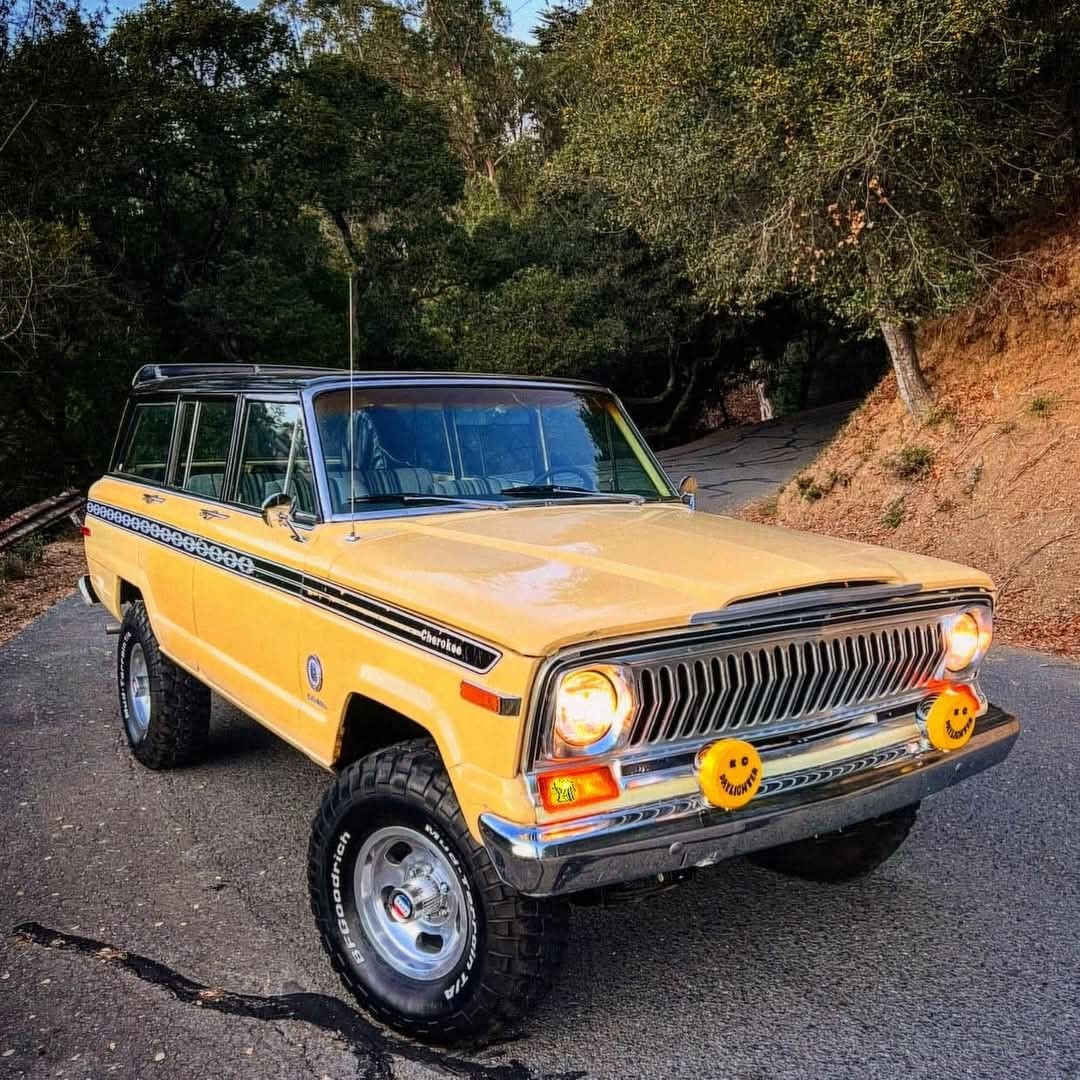 Classic yellow Jeep Wagoneer with white top on tree-lined road