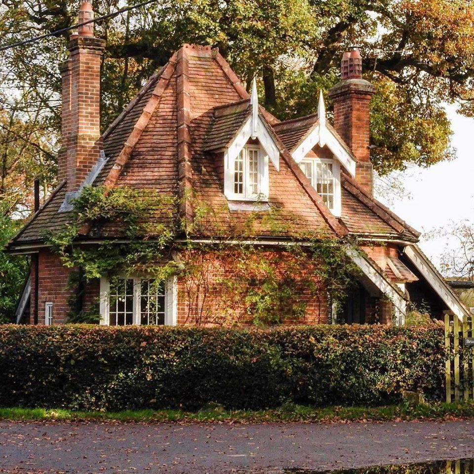 Quaint brick cottage with ivy, steep roof, ornate chimneys, and Gothic-style windows in autumn setting