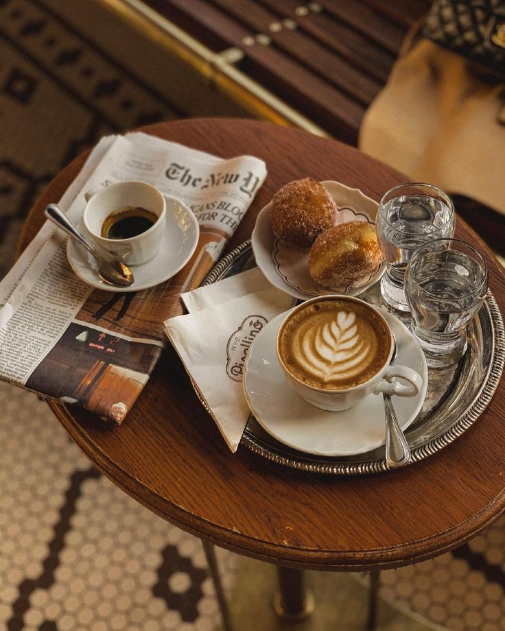 Overhead view of coffee drinks, croissant, and newspaper on round wooden cafe table