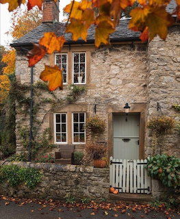Stone cottage with green door and white gate framed by fall leaves in orange and red