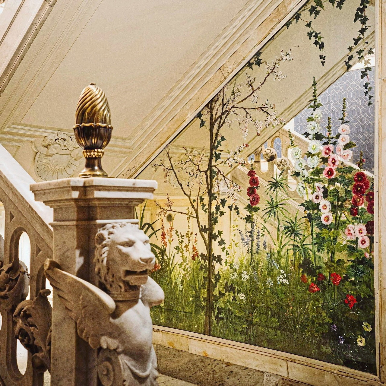 Marble staircase with lion sculpture and golden finial next to a colorful floral wall mural in a palace