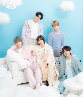 Five young men in pastel outfits sitting and standing on white furniture with cloudy sky background
