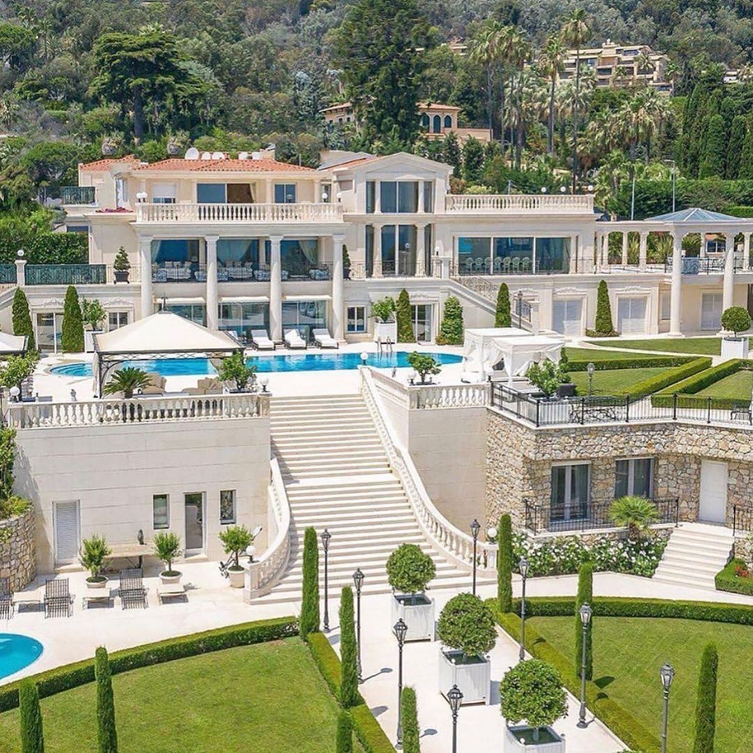 Aerial view of white luxury villa with pools and landscaped gardens against mountain hillside