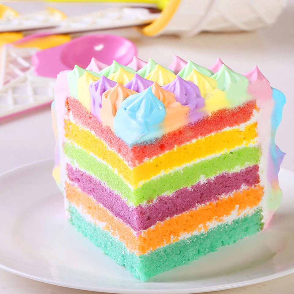 Slice of rainbow layer cake with colorful frosting swirls on white plate