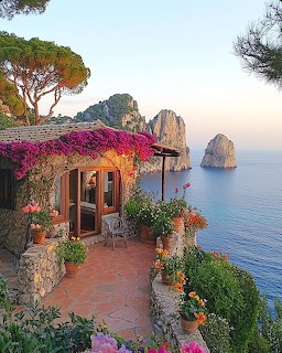 Flower-covered terrace on cliff edge overlooking blue Mediterranean sea and tall coastal rock formations at golden hour