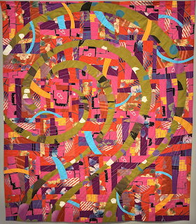 Colorful abstract quilt with geometric shapes and curved patterns in vibrant pink, orange, and red tones