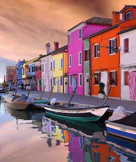 Brightly painted houses in pink, orange, yellow and blue along a canal with boats at sunset