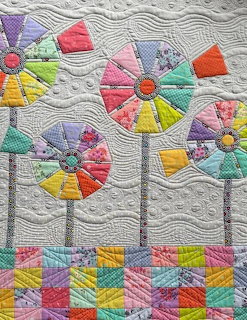 Patchwork quilt with colorful windmill flowers and geometric borders on gray background
