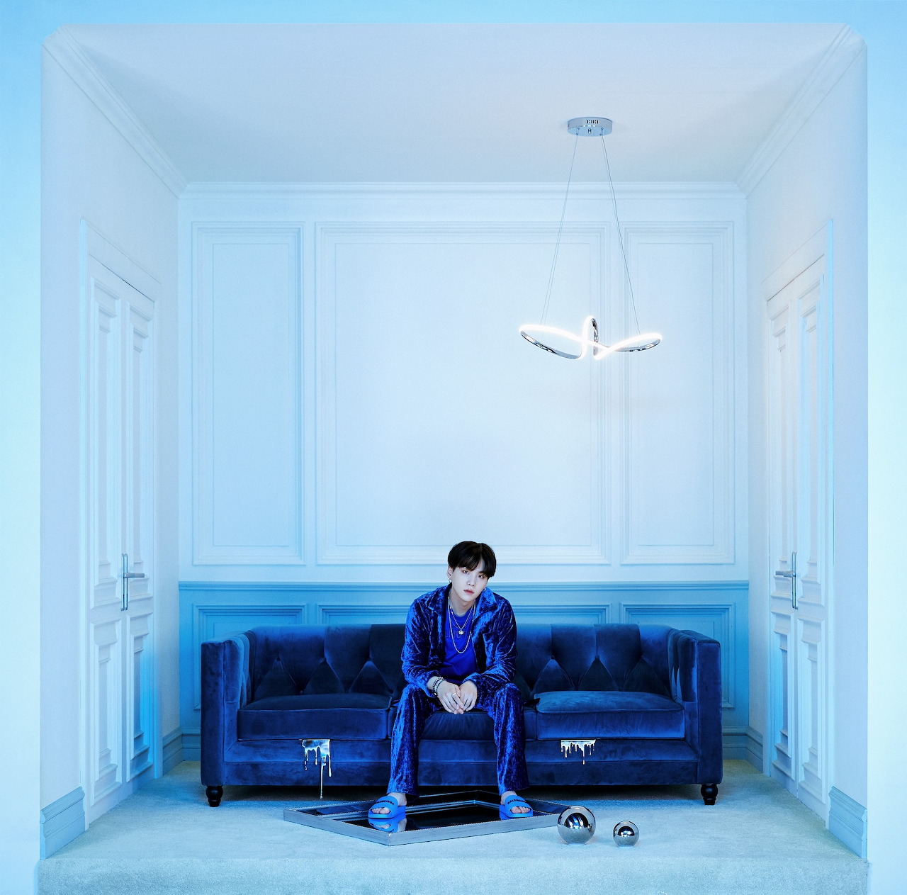 Man in a blue outfit sitting on a blue sofa in a pale blue room