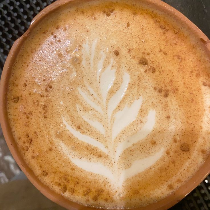Close-up of coffee with white foam fern leaf latte art and cinnamon in brown cup