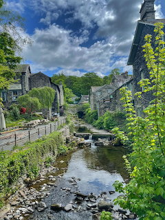 Stream flowing through Ambleside village with stone bridge, traditional buildings, and vibrant foliage under cloudy sky