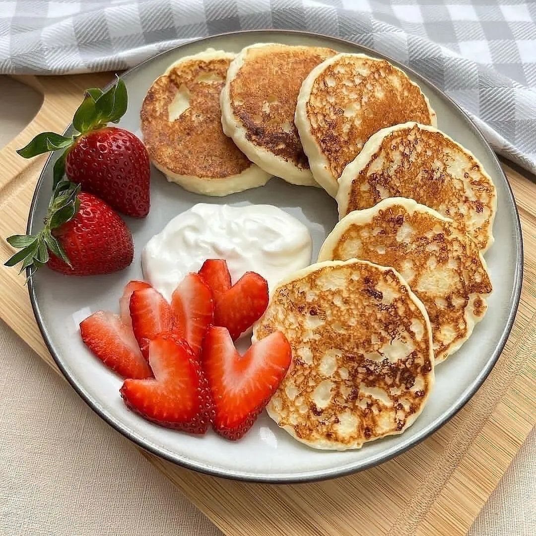 Circular arrangement of pancakes with strawberries and cream on white plate