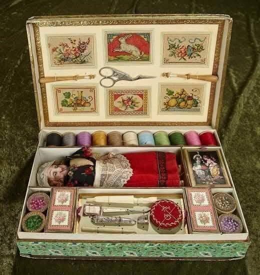 Open vintage sewing box with thread spools, scissors, buttons, lace and embroidered floral panels