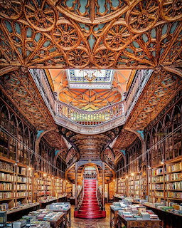 Ornate bookstore interior with intricate carved ceiling, red staircase, and wall-to-wall bookshelves