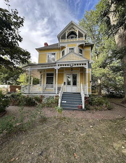 Yellow Victorian house with front porch, steps, and trees
