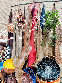 Leather skins and hides hanging at Moroccan market stall with colorful poufs and baskets below