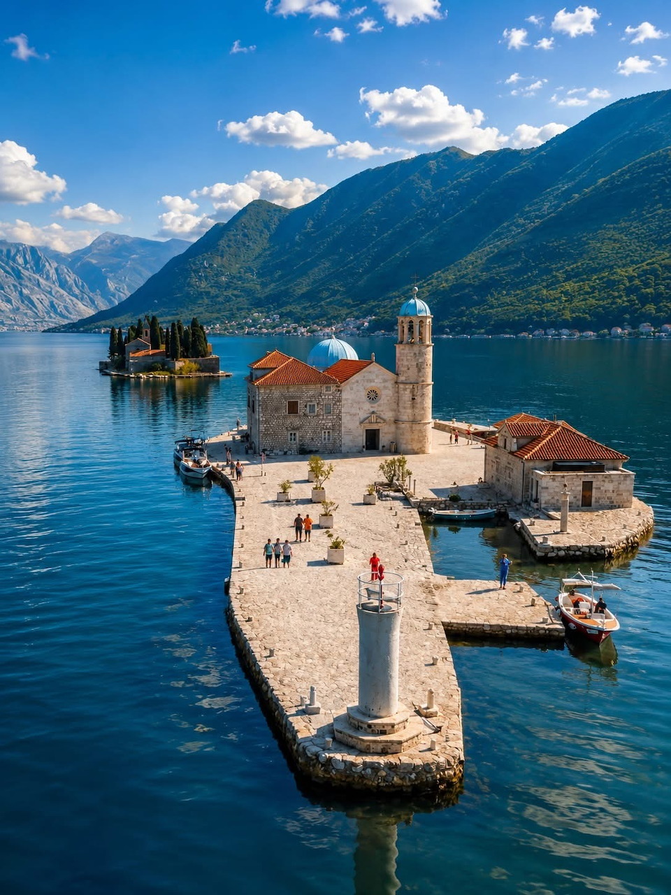 Stone church and small buildings on a tiny island in blue water with mountains behind