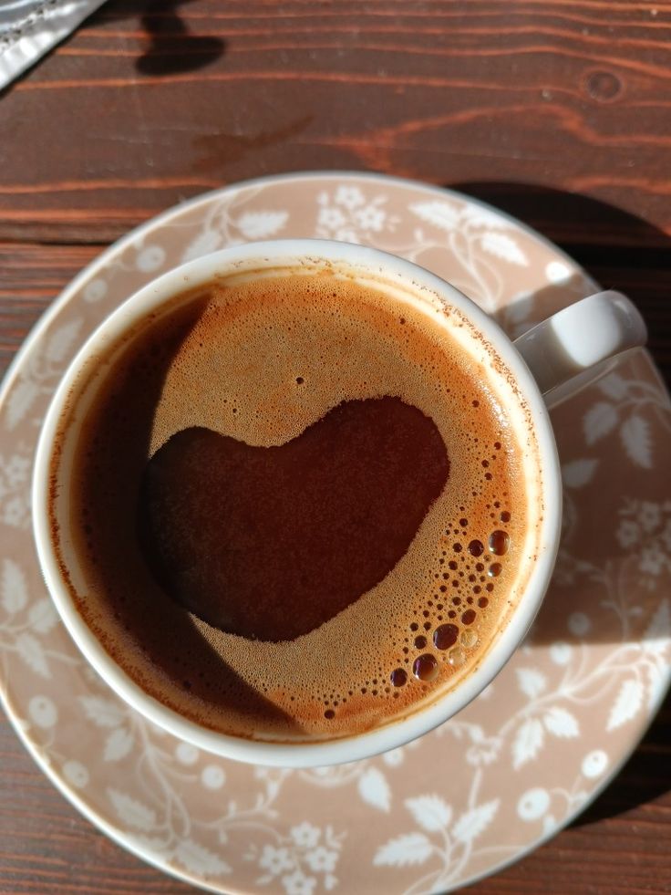 Coffee cup with heart latte art on floral saucer, wooden table background