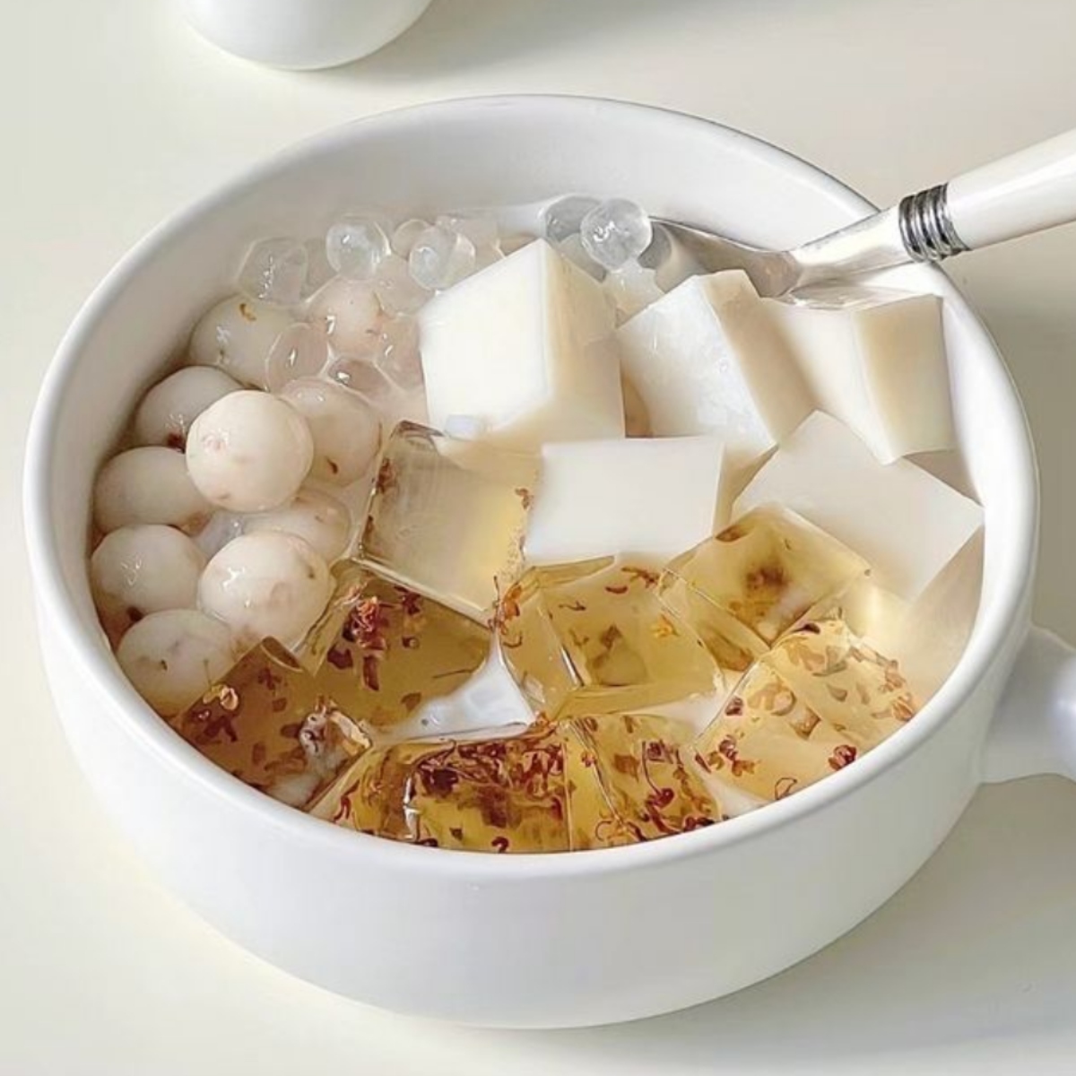 Bowl of Asian dessert with sago pearls, white jelly cubes, and golden flakes in milky liquid