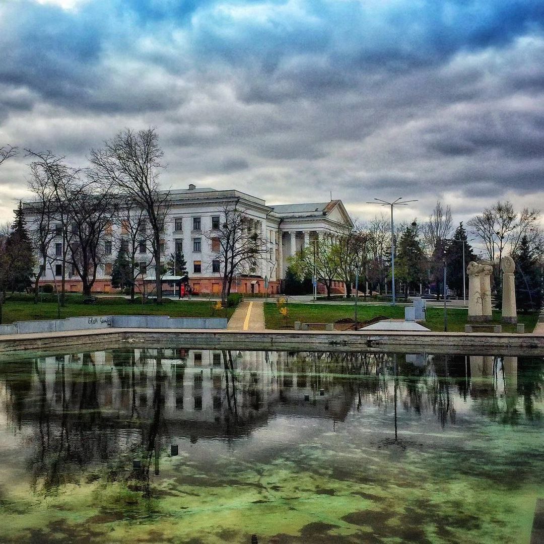 White neoclassical building reflected in a pond under dark cloudy skies
