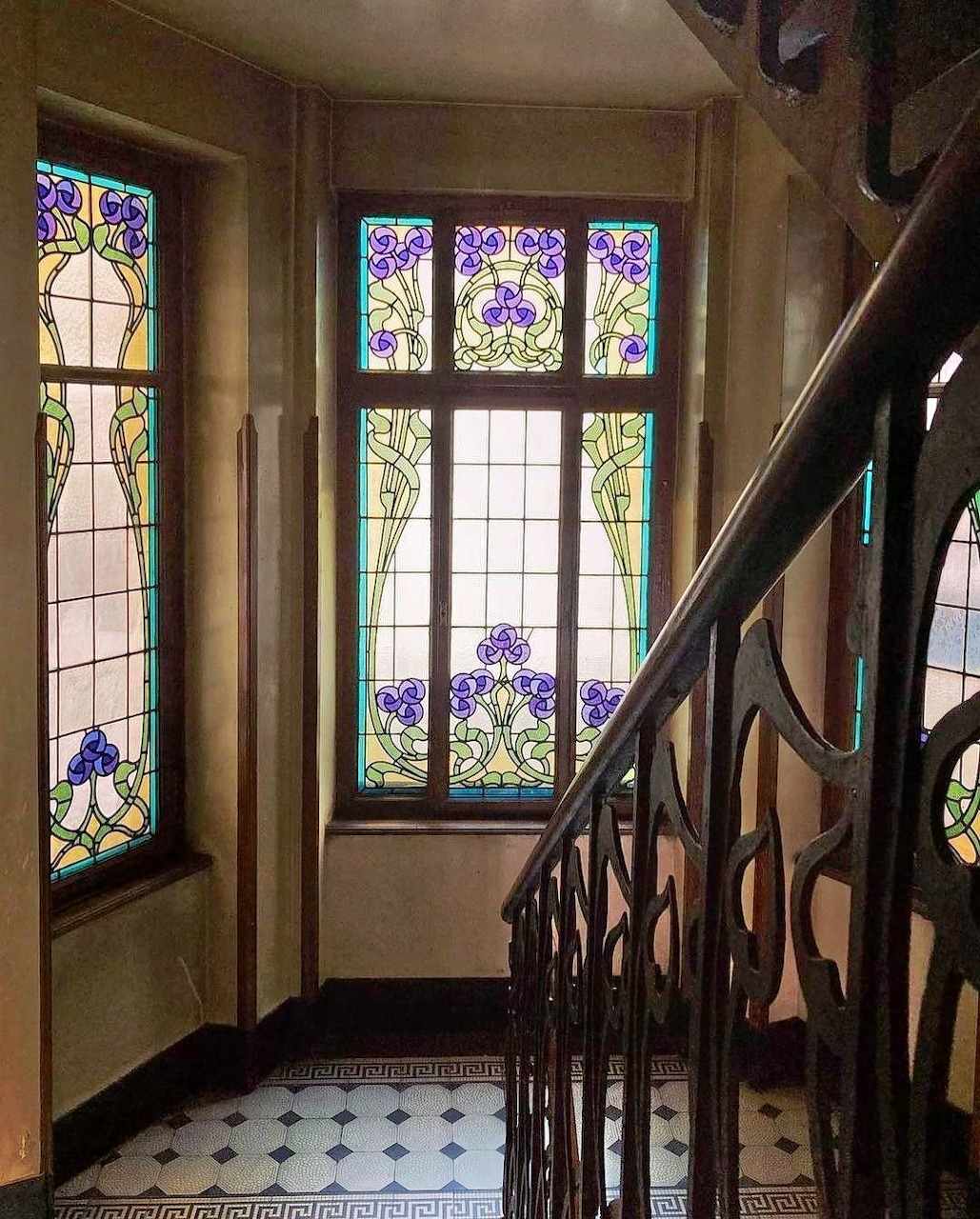 Art Nouveau staircase with carved wood railing and colorful stained glass windows showing purple iris flowers
