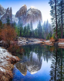 Mountain cliffs reflecting in still river with trees along rocky shore