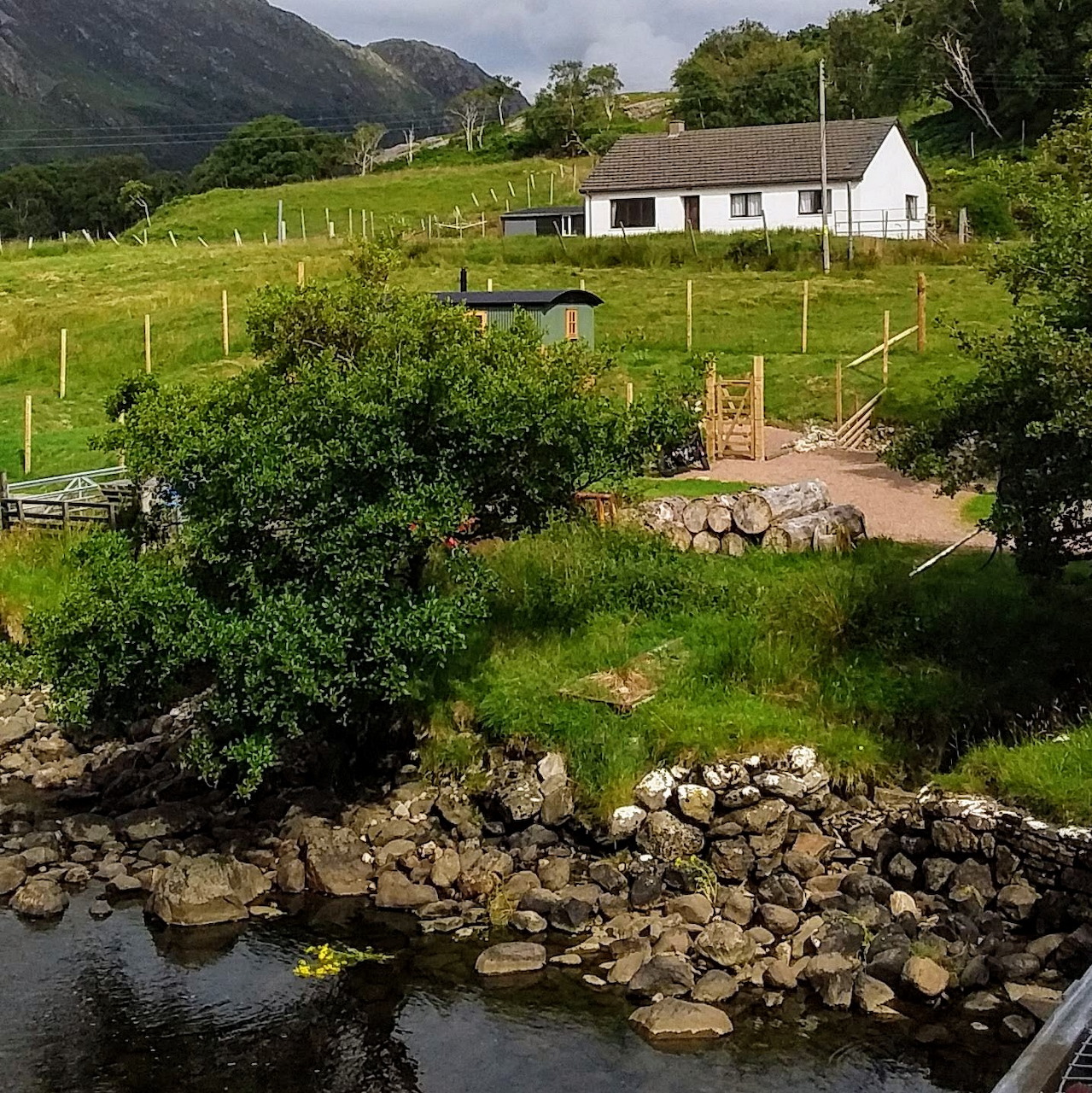 White cottage beside stone bridge crossing stream in green Scottish Highland valley with mountains