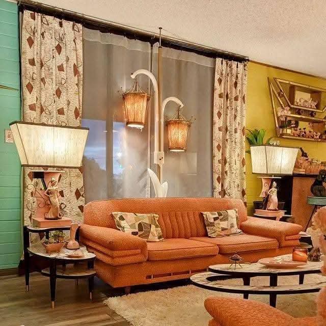 Vintage living room with orange sofa, lamps, curtains, and wall shelves
