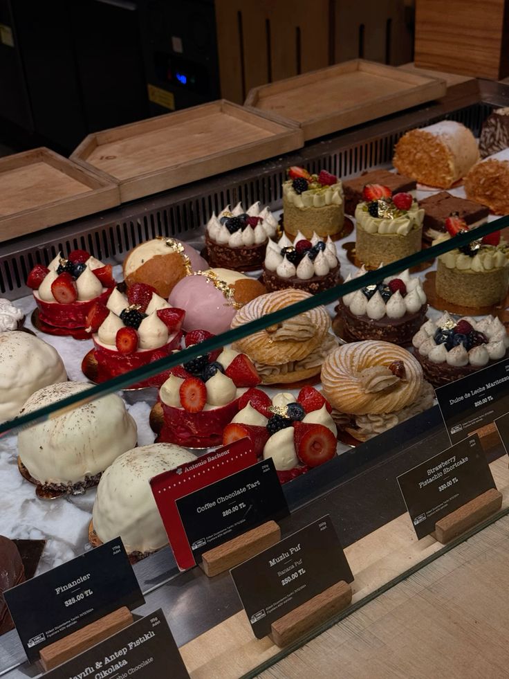 Glass display case with assorted pastries, cream cakes, tarts, and fruit-topped desserts at a bakery