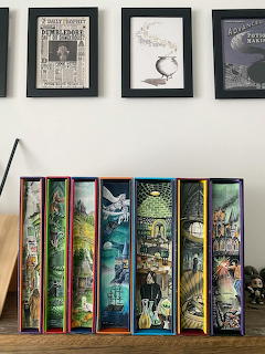 Decorative books with colorful illustrated spines arranged on shelf below framed prints