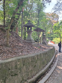 Stone lantern in Japanese garden with curved wall, trees, and walking path