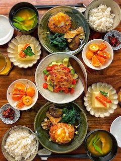 Top-down view of a Japanese meal spread with multiple dishes including rice, soup, salad, and fruit on a wooden table