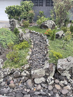 Aerial view of a garden with a winding dark rock stream path surrounded by plants and stone borders