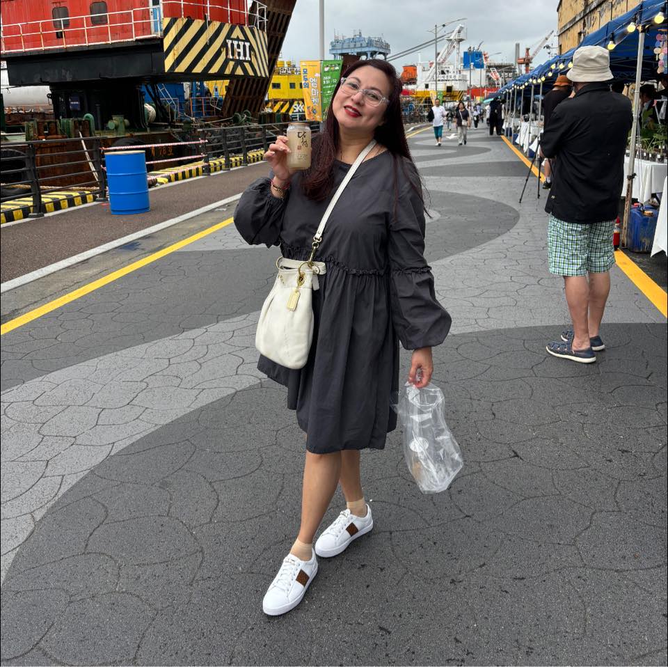 Woman in black dress posing on street at harbor with ships in background