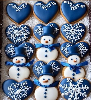 Blue and white frosted cookies shaped as snowmen, hearts, and snowflakes on wood background