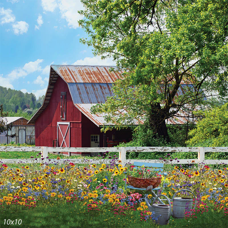 Red barn behind a white fence with colorful wildflowers and a large tree under a blue sky