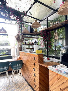 Cozy café interior with wooden counter, glass roof draped in pink flowers, and hanging wicker lamps